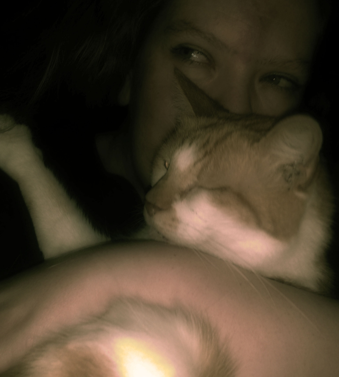 A sepia toned image of a woman snuggling with an orange and white cat.